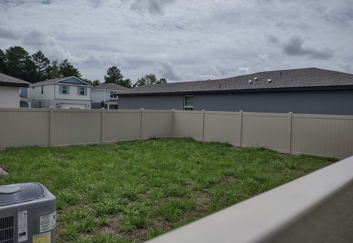 Tan vinyl privacy fence enclosing a backyard